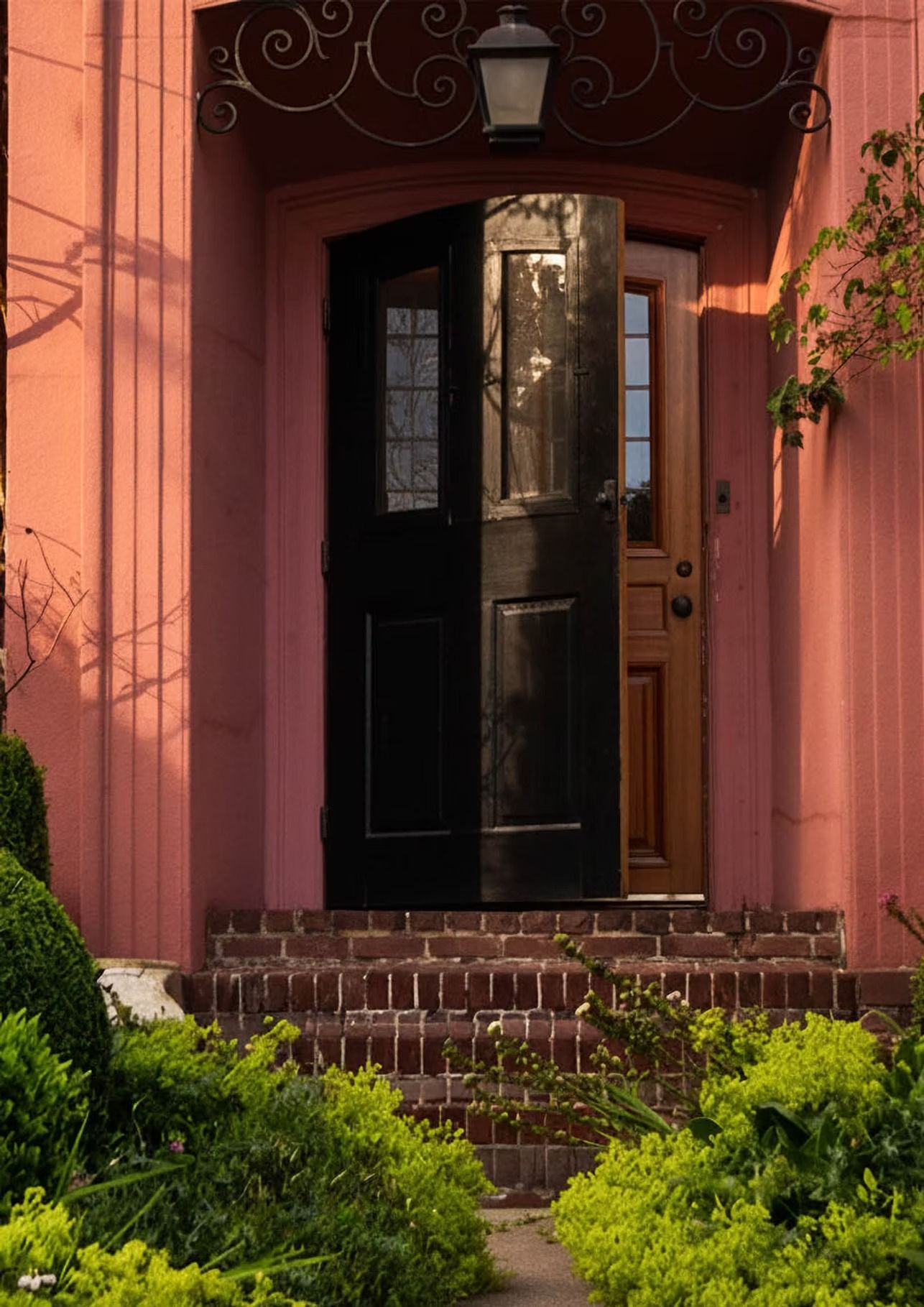 Red brick steps lead to open black door, framed by red walls and topped with a wrought iron design.