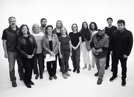 Group of people posing together, all facing forward. Black and white, studio setting.