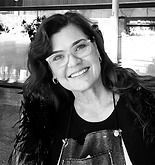 Woman smiling, wearing glasses and black clothing, in a cafe setting.