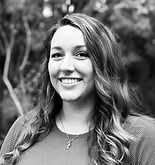 Smiling woman with long wavy hair, wearing a dark top, outdoors.
