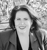 Woman with dark hair, smiling, wearing a jacket, with a floral background.