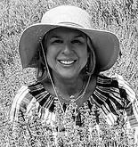 Woman wearing a hat smiles, in front of a natural background.