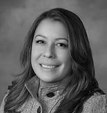 Woman with long hair smiles, wearing a patterned jacket, in a grayscale portrait.