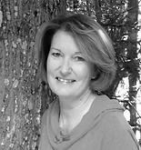 Woman smiling, leaning against a tree in an outdoor setting.