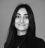 Woman with long dark hair smiles, wearing a black turtleneck and a necklace, against a neutral background.