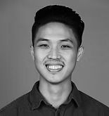 Smiling man with dark hair in a button-down shirt, headshot against a gray background.