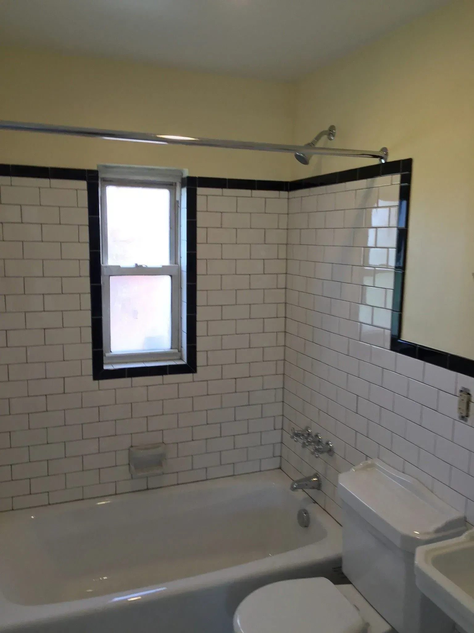 A white-tiled bathroom with a tub, toilet, and window.