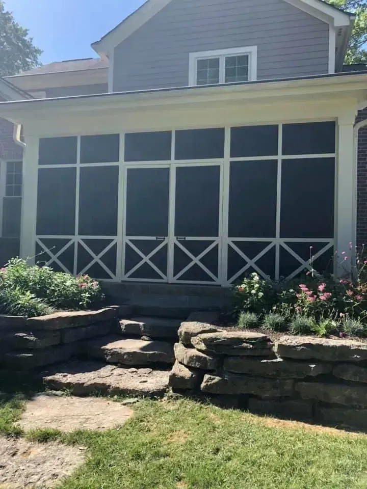 Screened porch with white trim, stone steps, and a rock retaining wall with greenery.