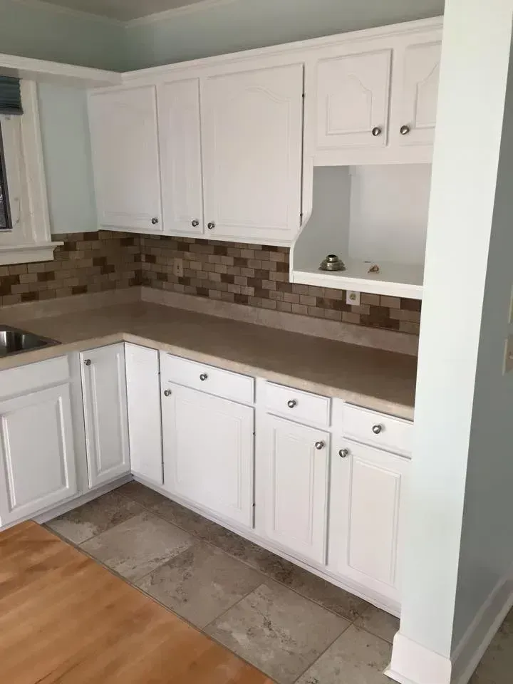 White kitchen cabinets with a light brown countertop and a mosaic tile backsplash.