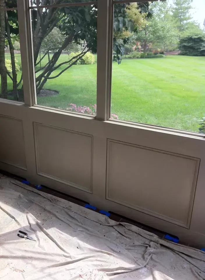 Cream-colored wall paneling with a window above it, overlooking a green lawn.