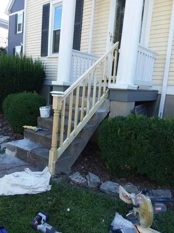 A porch with steps has new, light-colored wooden railings.