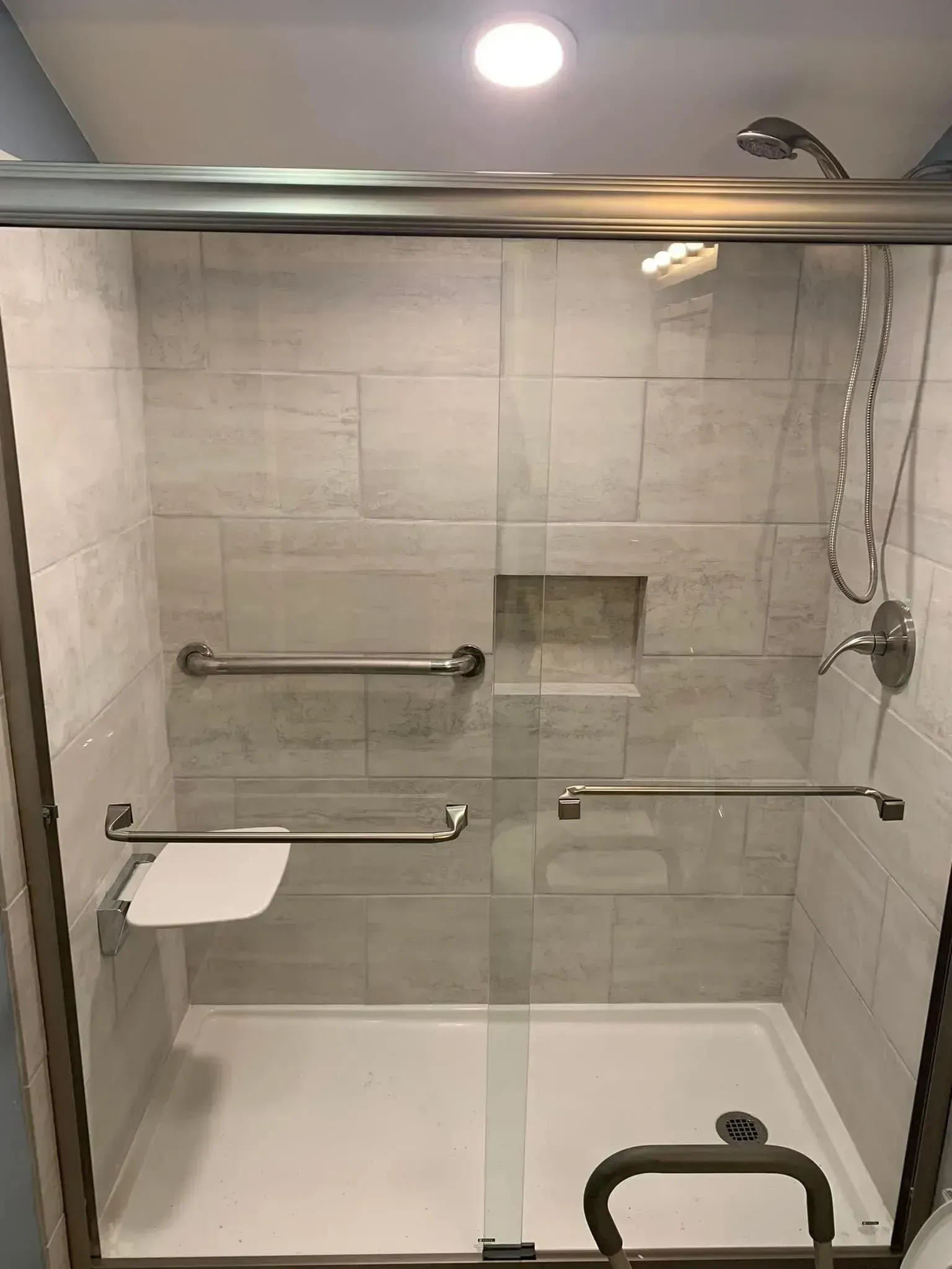 A shower stall with light-colored tile, a built-in seat, grab bars, and a sliding glass door.