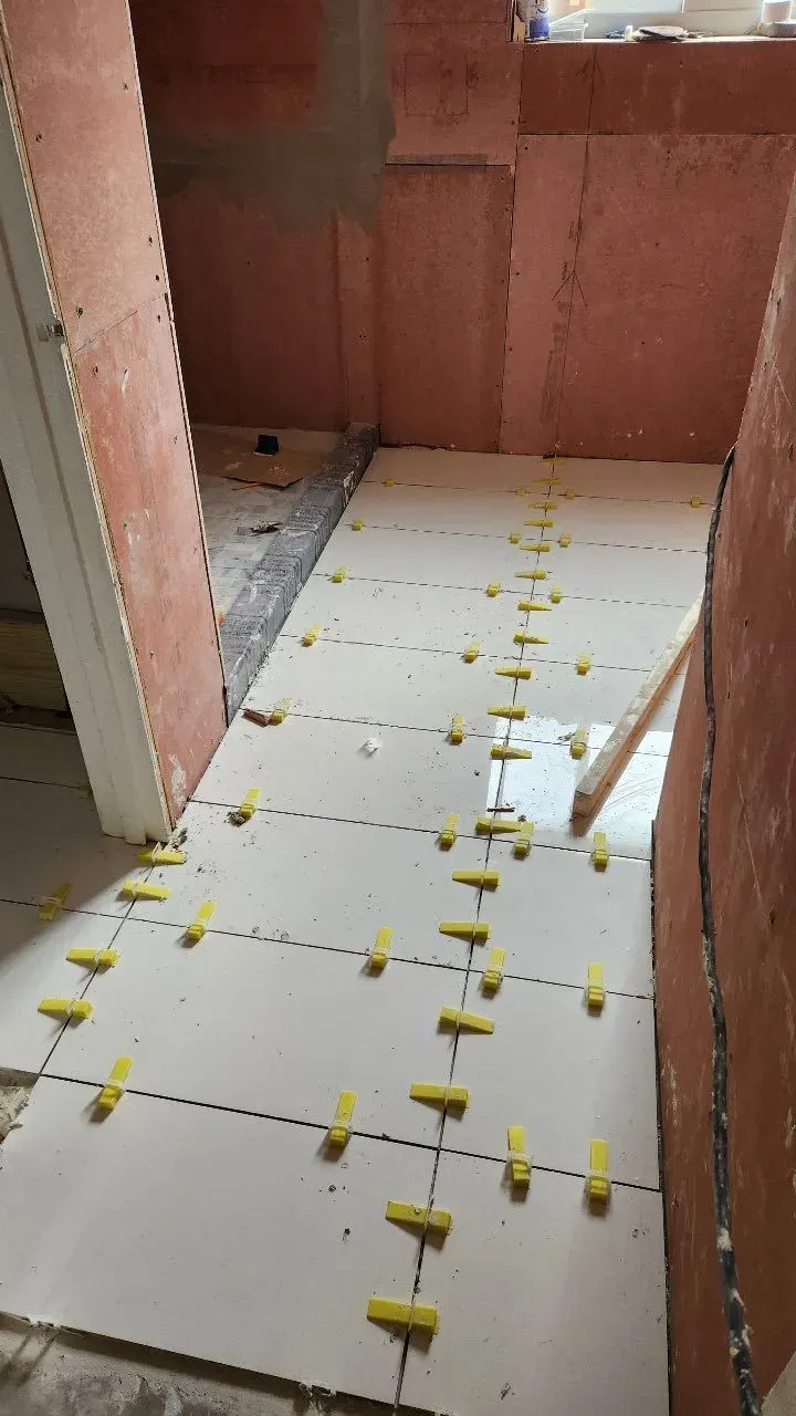 Tiles being installed on a floor, with yellow leveling clips in between. Interior construction setting.