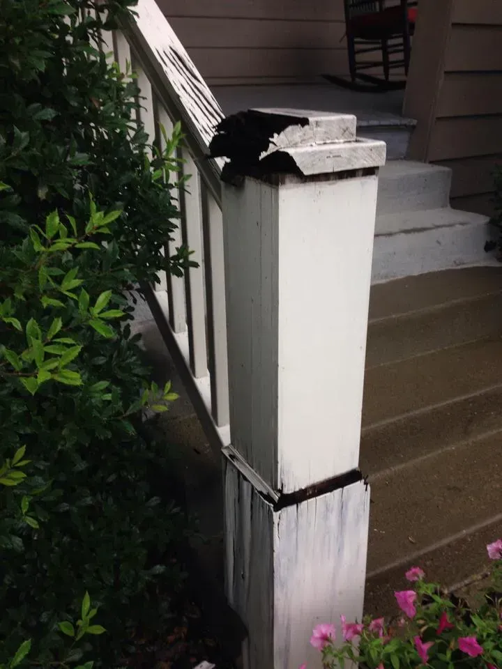 A black cat is sitting on top of a white railing