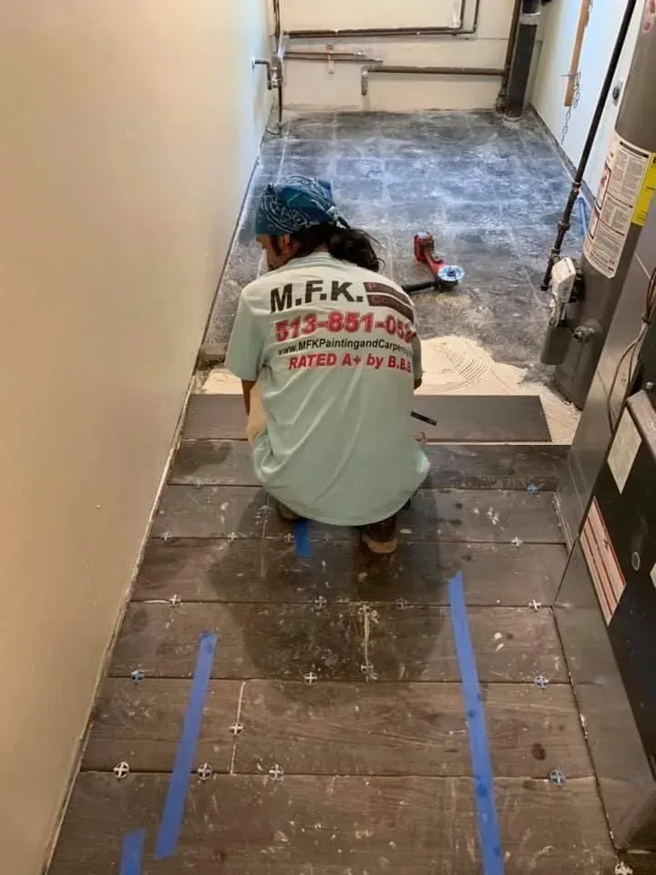 A man is kneeling down on a tiled floor in a hallway.