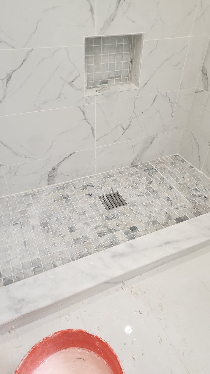 A bathroom with a walk in shower and a drain.
