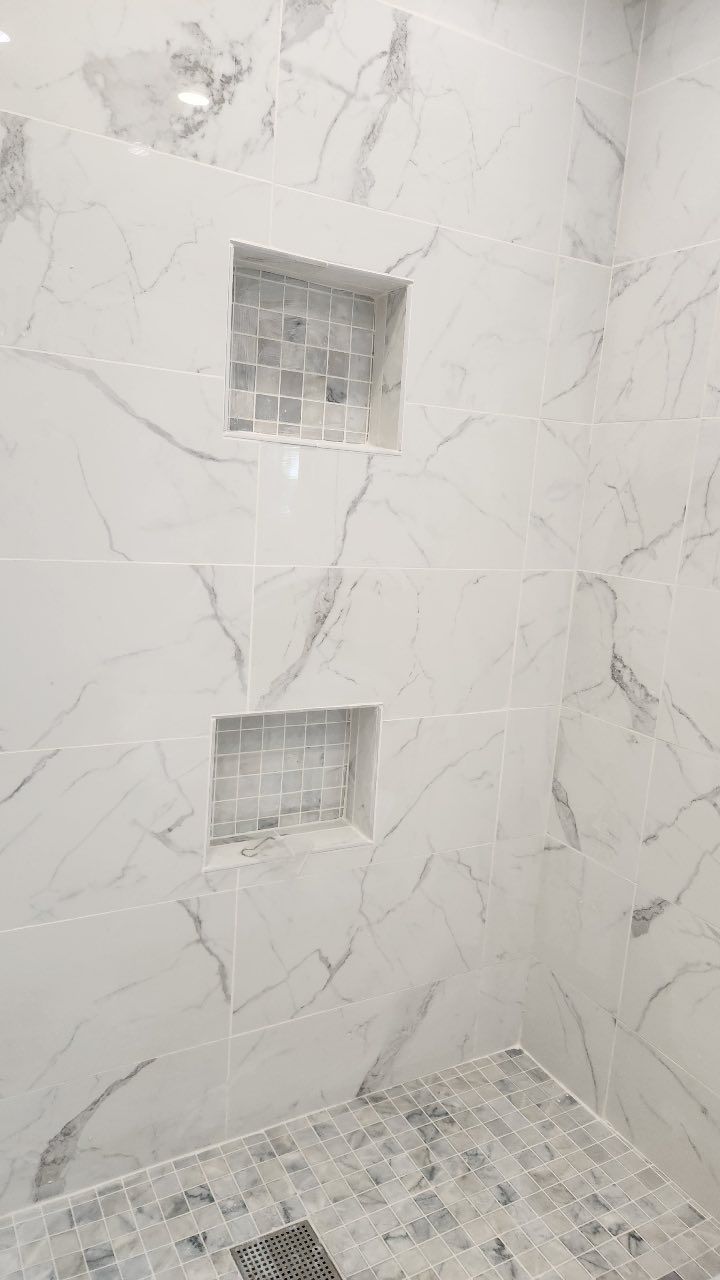 A shower with marble tiles and two niches on the wall.