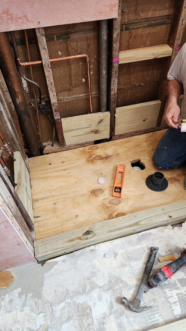 A man is kneeling on a wooden floor in a bathroom.