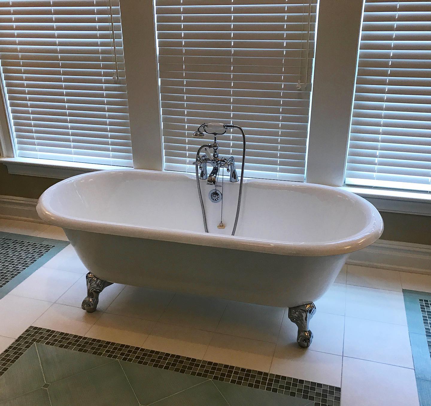 A bathtub is sitting in a bathroom next to a window with blinds.