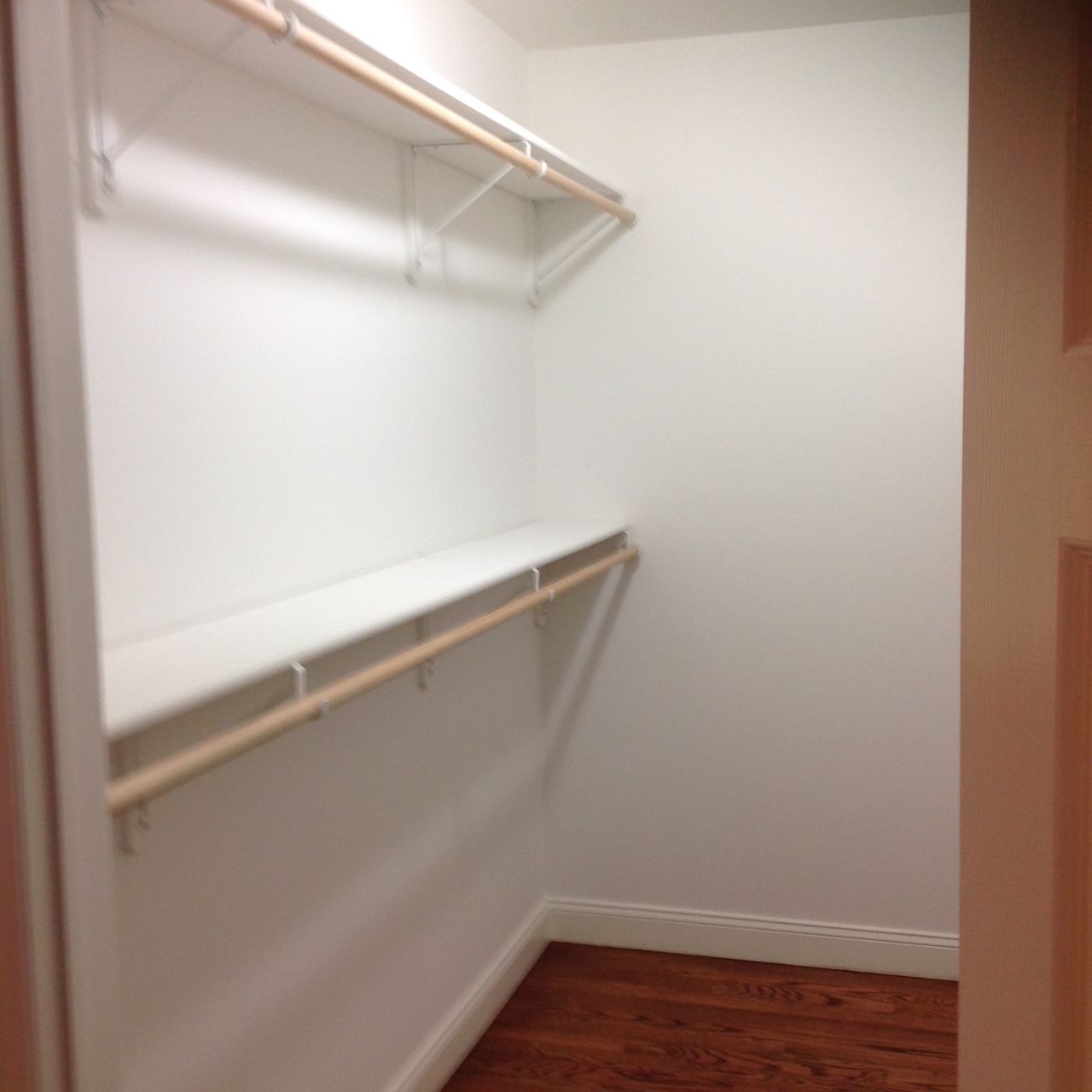 A walk in closet with a wooden floor and white shelves