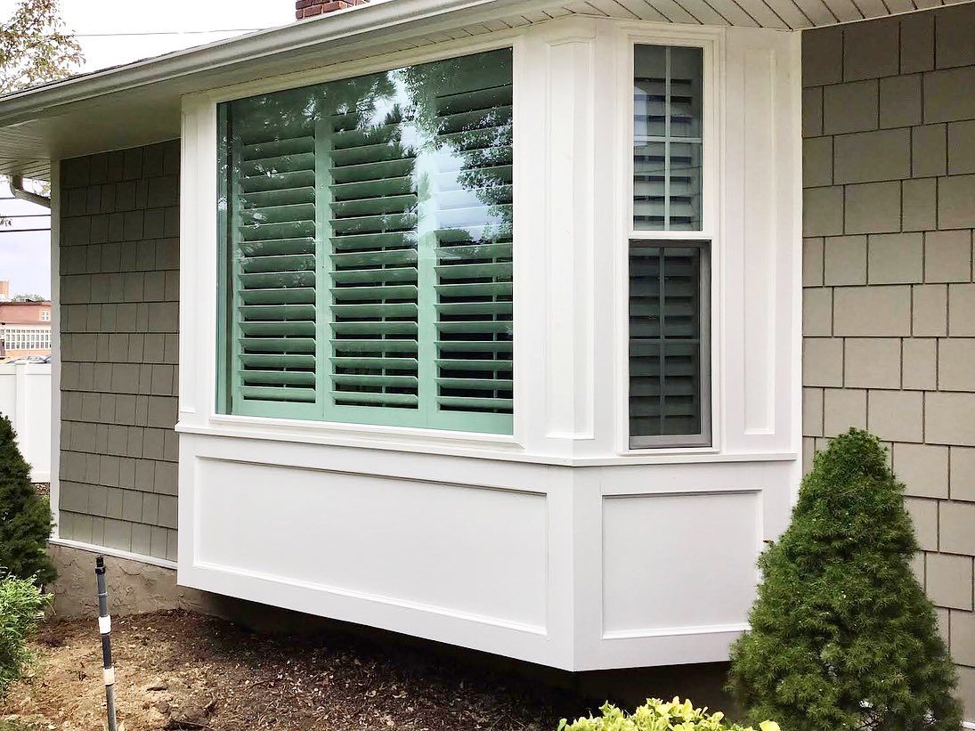 A white house with a bay window and green shutters.