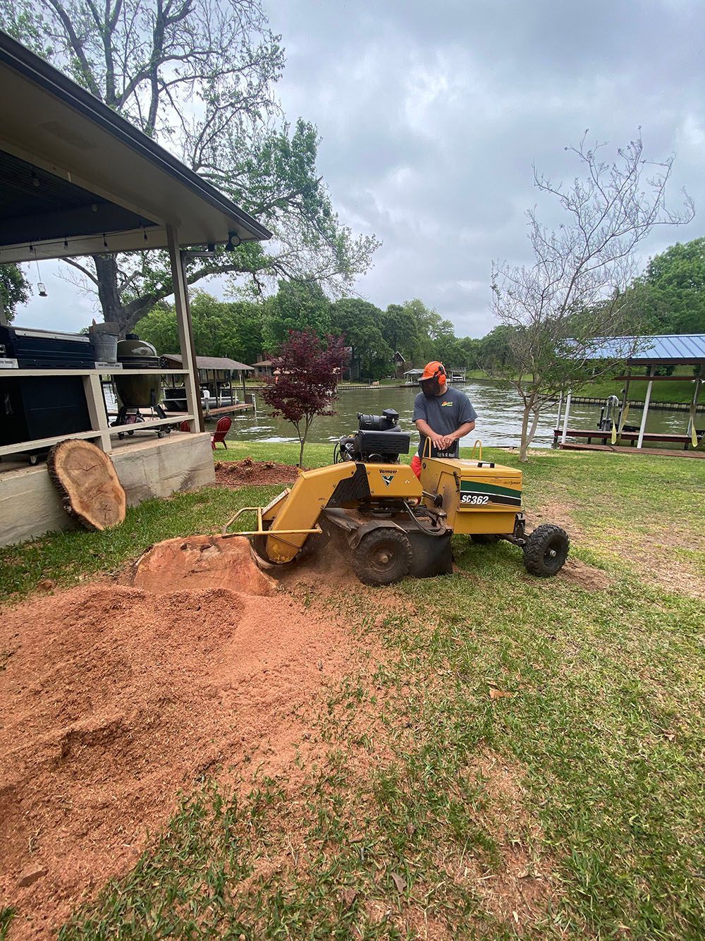 Person operating a yellow wood chipper beside a pile of wood chips near a shed outdoors