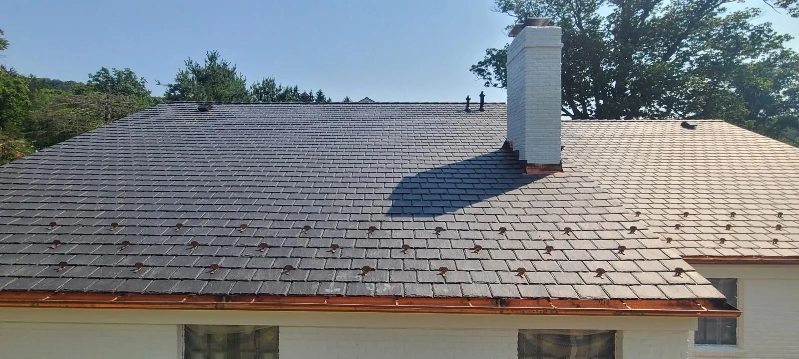 A house roof showing a stark contrast between cleaned, lighter shingles and dark, mossy, or stained ones near a chimney.