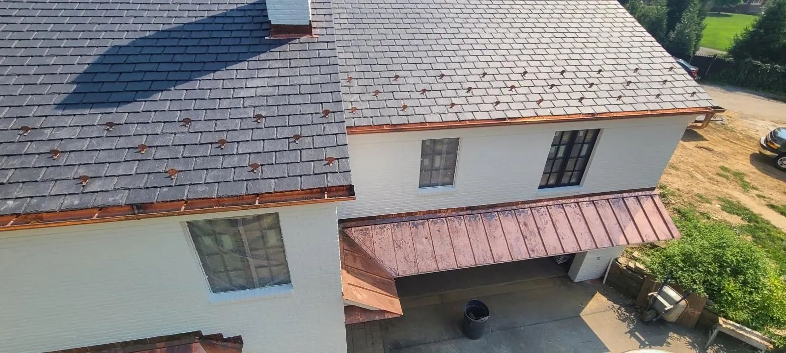 High-angle shot of a house with slate roof tiles, copper flashing, and a copper-roofed porch extension over the driveway.