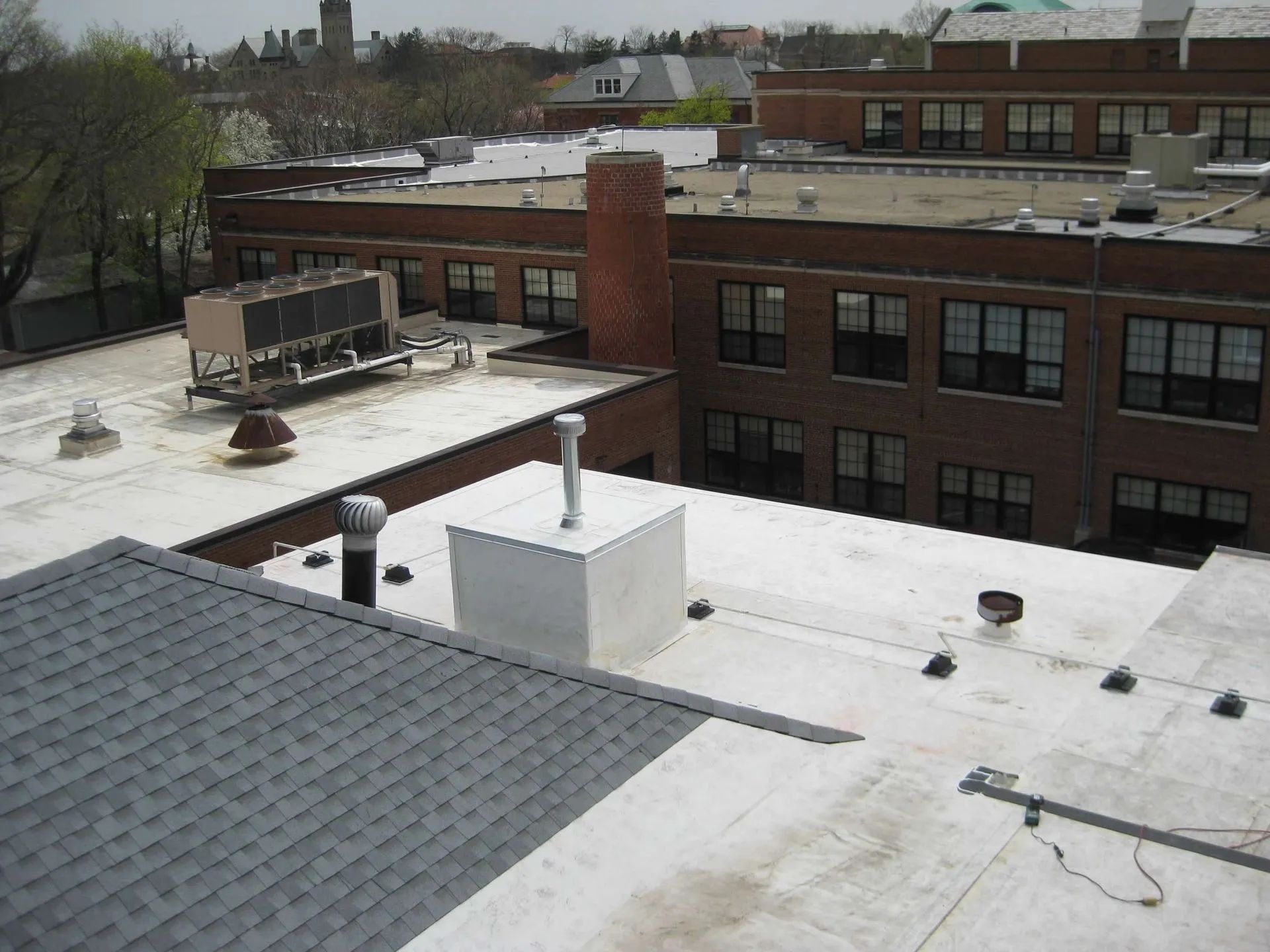 An elevated view of a flat white roof with mechanical equipment, adjacent to a brick building with windows.