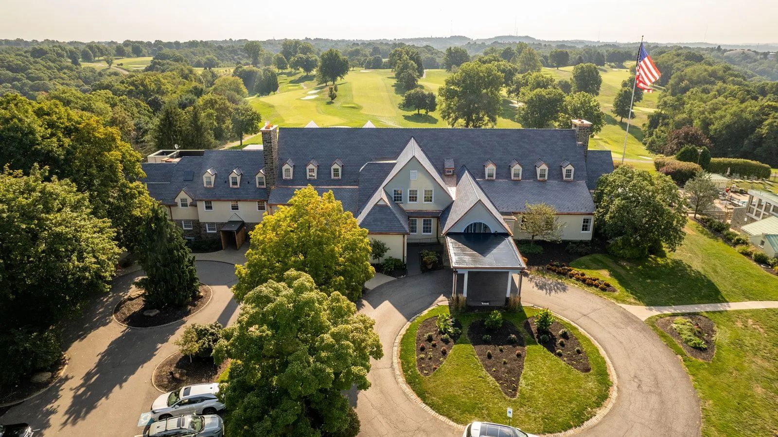 Aerial view of a large, multi-story country club building with a stone exterior and blue roof, surrounded by a golf course.