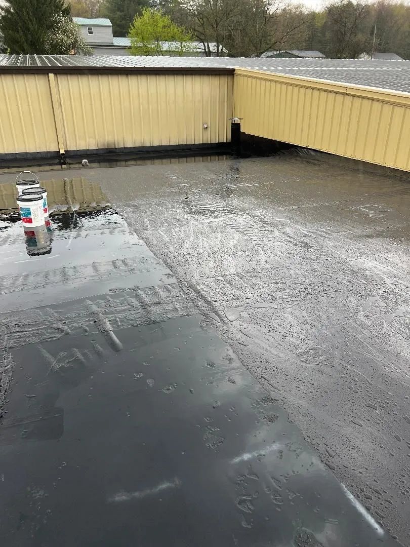 A flat, tar-coated commercial roof with standing water and yellow metal walls in the background.