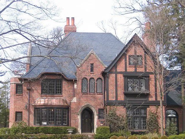 A stately, multi-story brick Tudor-style home with a slate roof, prominent chimneys, and dark wood-trimmed windows.