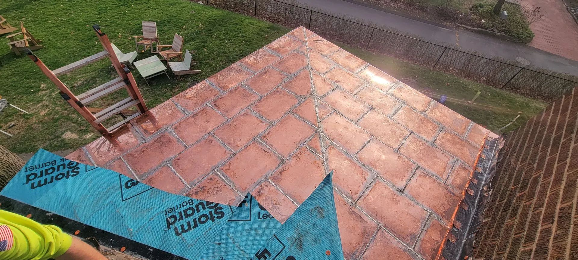 A view from above showing a roof partially covered in new, reddish-brown rectangular tiles, with a ladder to the left.