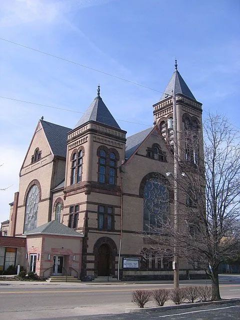 A beige brick church with two towers and stained-glass windows under a blue sky.
