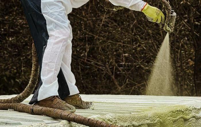 A man in a protective suit is spraying foam on a concrete surface.