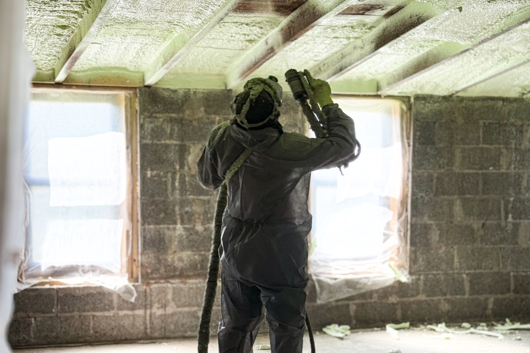A man is spraying foam on the ceiling of a room.