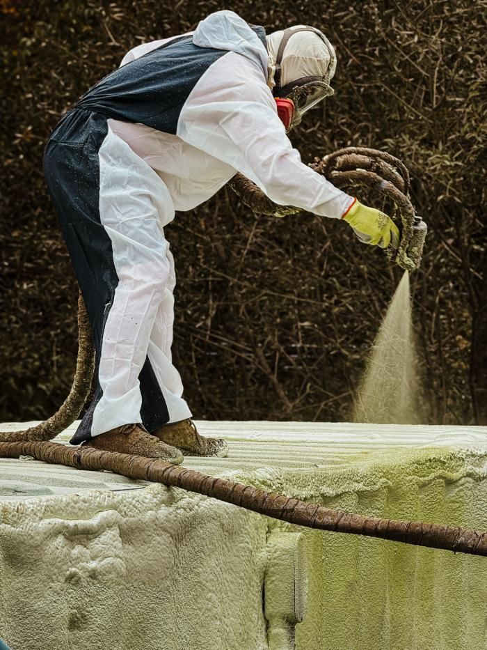 A man in a protective suit is spraying foam on a concrete surface.