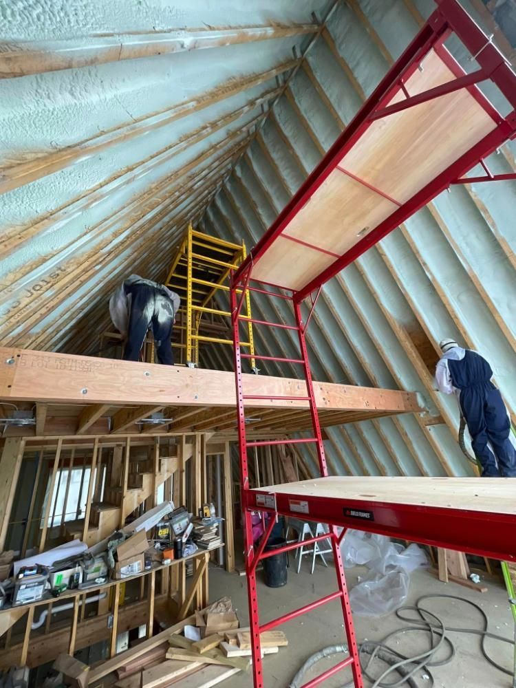 A man is standing on top of a scaffolding in an attic.