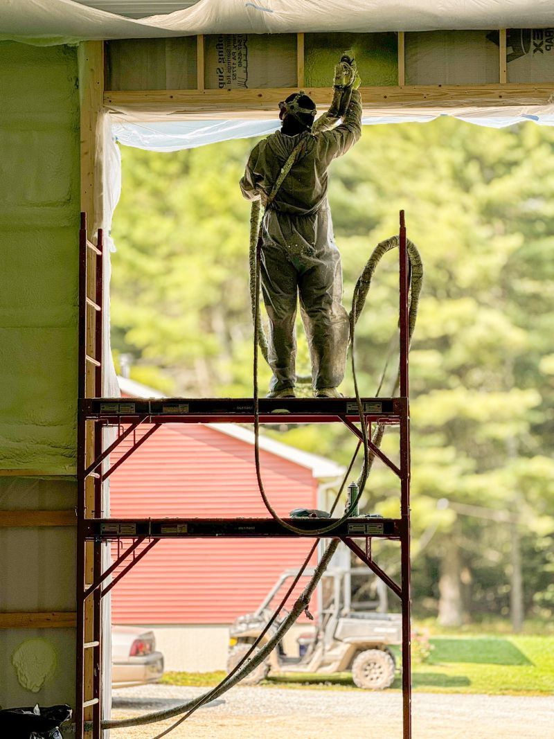 A man is spraying insulation on the ceiling of a garage door.