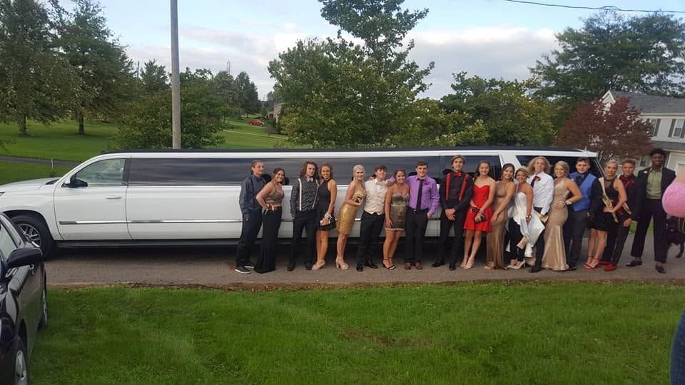 Group posing beside a white limousine on a suburban street, dressed in formal attire.