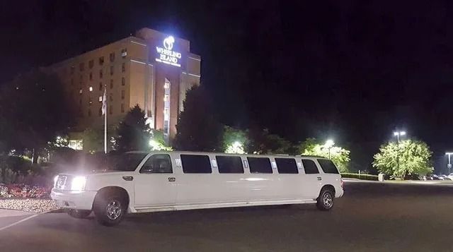 White stretch limousine parked at night in front of a lit hotel building.