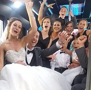 Bride and guests celebrating on a party bus, smiling and waving in formal wear