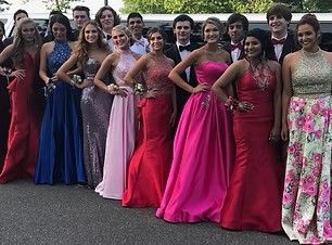Group of people in formal gowns posing outdoors, with bright pink, blue, and floral dresses.