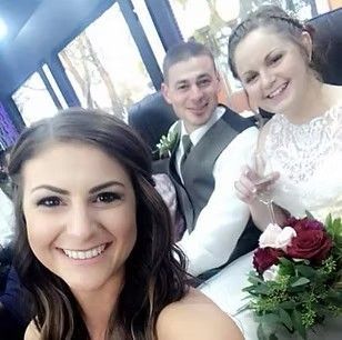Three smiling wedding guests pose for a selfie, with the bride holding a bouquet.