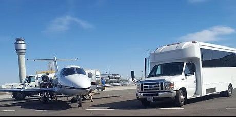 Small jet and white shuttle bus on airport tarmac near control tower under a clear blue sky
