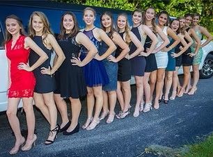 Group of women posing in dresses and heels outdoors along a driveway