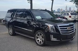 Black Cadillac SUV parked near the waterfront with city skyline in the background