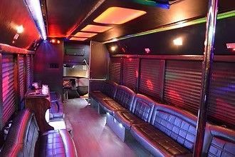 Empty party bus interior with black and red seating, neon ceiling lights, and tinted windows