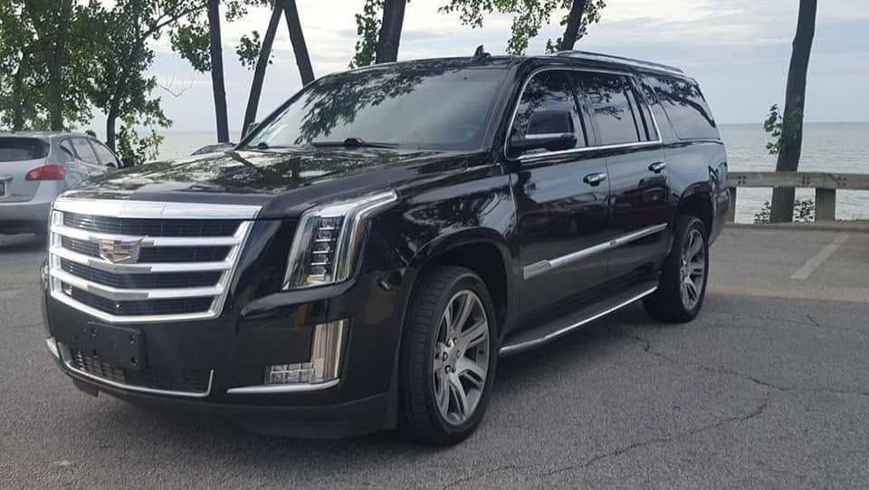 Black Cadillac Escalade SUV parked by a roadside with trees and water in the background