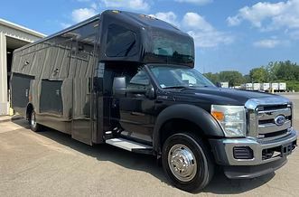 Black Ford expedition truck with a camper body parked on a sunny lot.